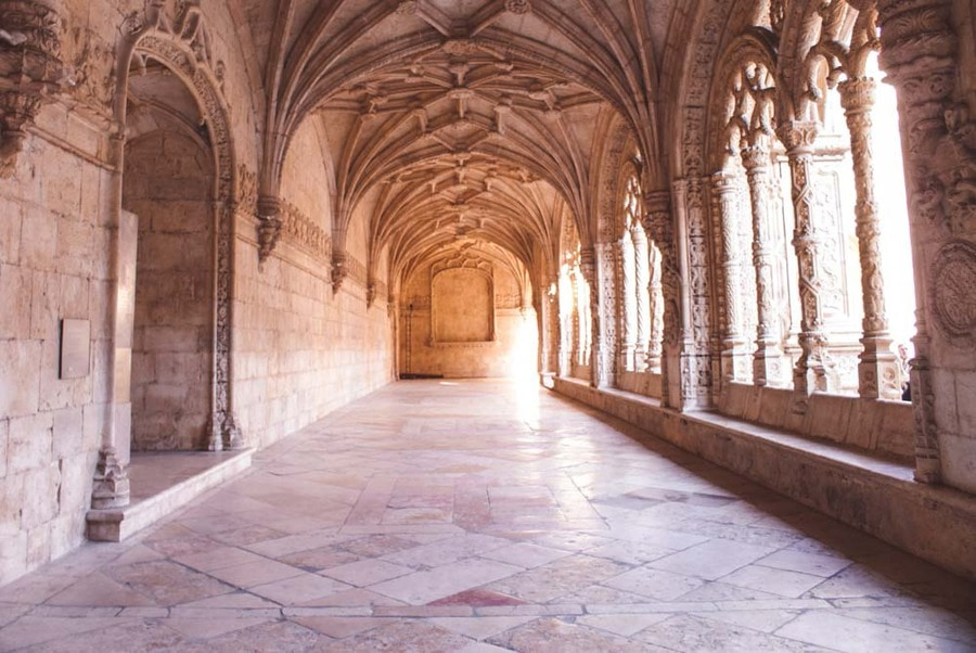 Sunlit vaulted walkway and carved stone arches inside the cloister of the Jerónimos Monastery in Belém, Lisbon