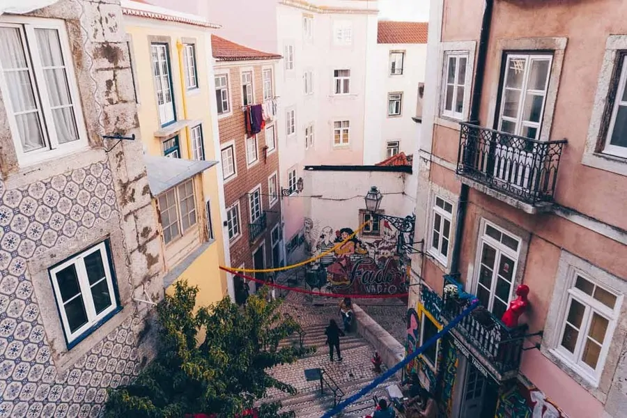 Tiled and pastel-painted houses with iron balconies around a stepped lane in Lisbon's old quarter