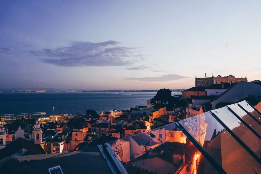 Terracotta rooftops and a church tower running down to the River Tagus at dusk in Lisbon's old town