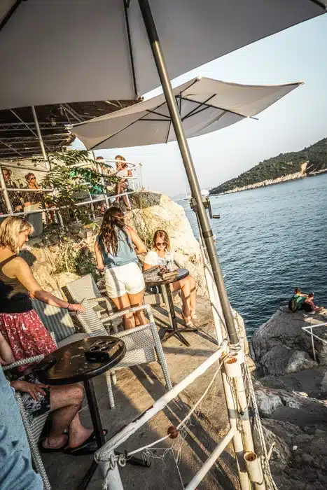 Terraced drinking area at Buza Dubrovnik - Buza Bar is one of Dubrovnik's coolest nightlife spots. This cliffside bar bosts beautiful views of the sea from a hidden spot in Dubrovnik Old Town. One of the top things to do in Dubrovnik! Read now #dubrovnik #travel #wanderlust