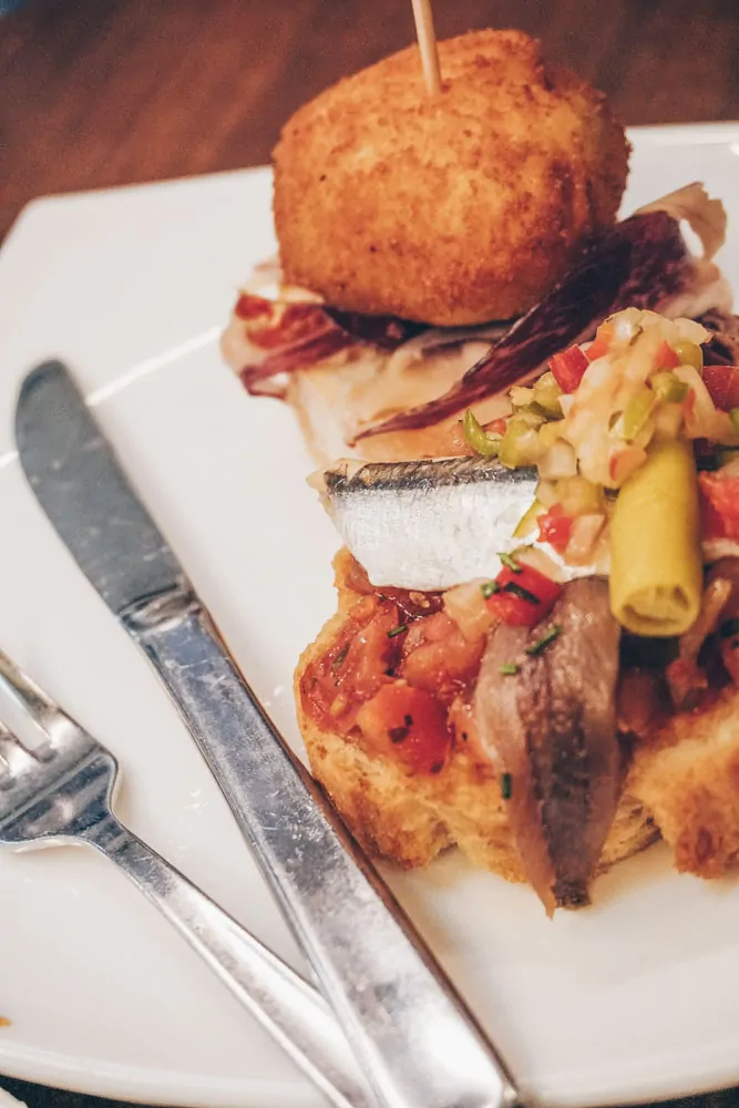 A tall pintxo topped with a fried croquette and peppers on a plate at Artxanda Jatetxea, Bilbao