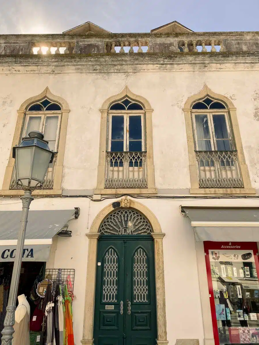 White townhouse with ornate arched windows, iron balconies and a green panelled door above a shopfront in the old town of Lagos