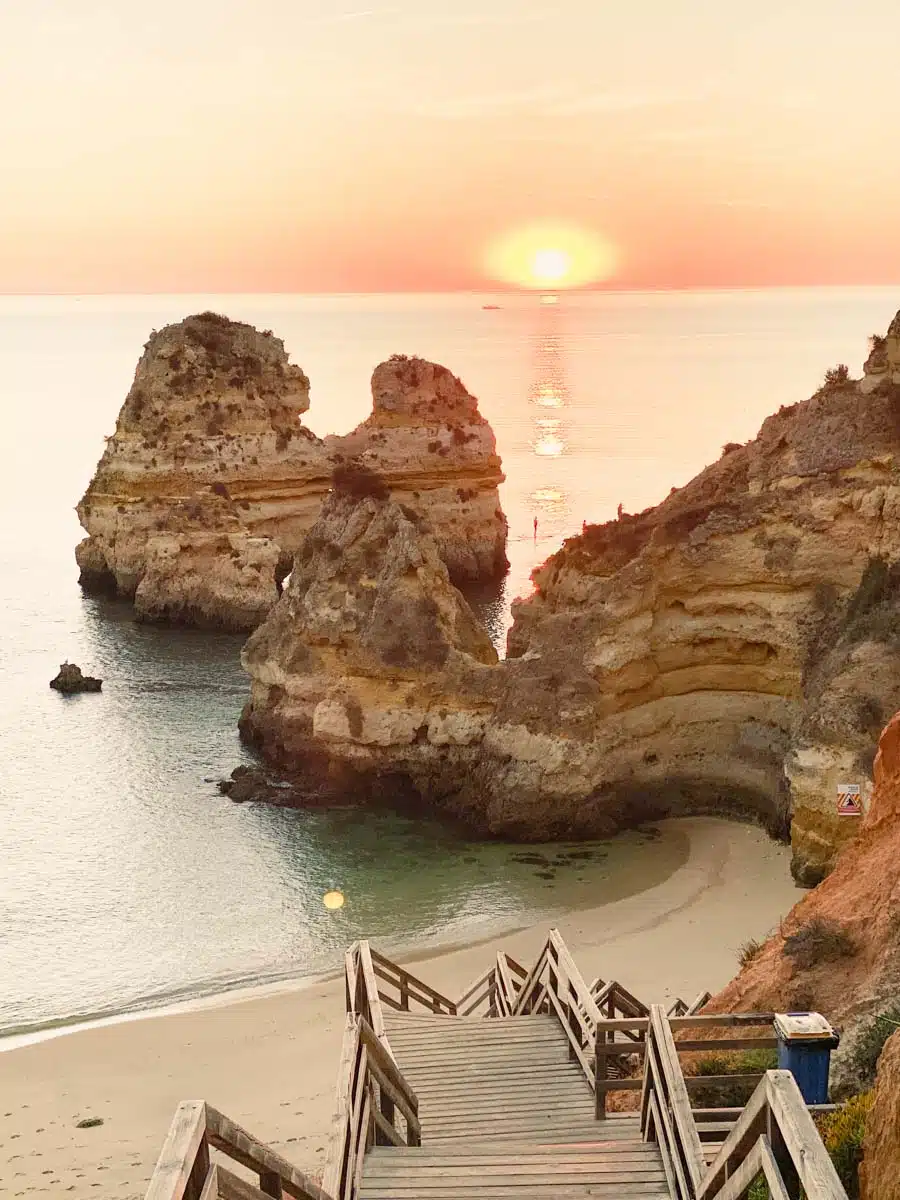 Wooden staircase zigzagging down the cliff towards Praia do Camilo near Lagos, with golden rock stacks and a low sun over the sea