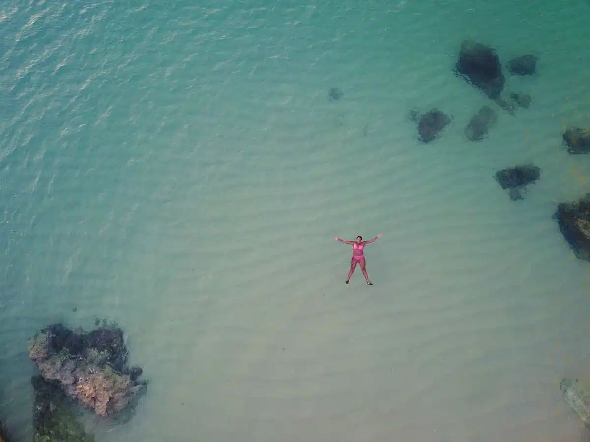 Aerial drone view of a swimmer floating in clear turquoise water over dark rocks off the western Algarve coast