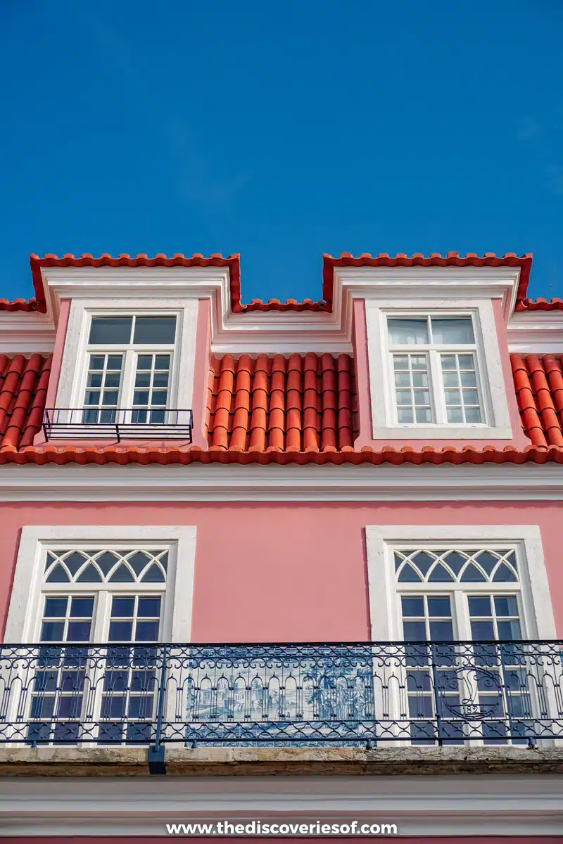 A pink house with white window frames, a red tiled roof and wrought-iron balconies in Mouraria, Lisbon