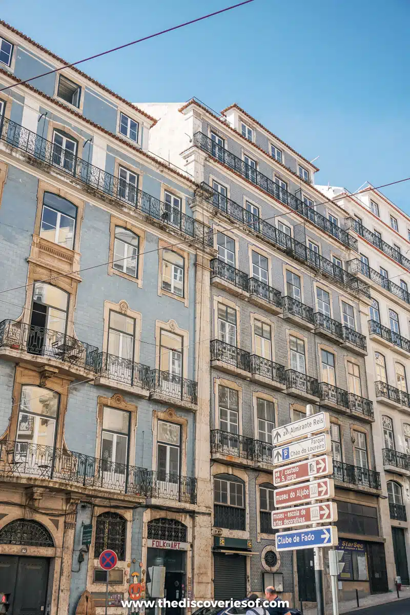 Tall pastel blue apartment buildings with iron balconies and street signs on a corner in central Lisbon