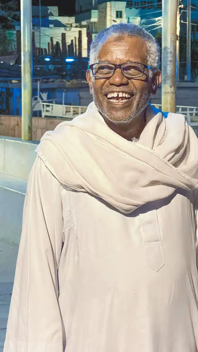 A smiling Nubian man in a white galabiya, host of a family dinner in a Nubian village near Aswan