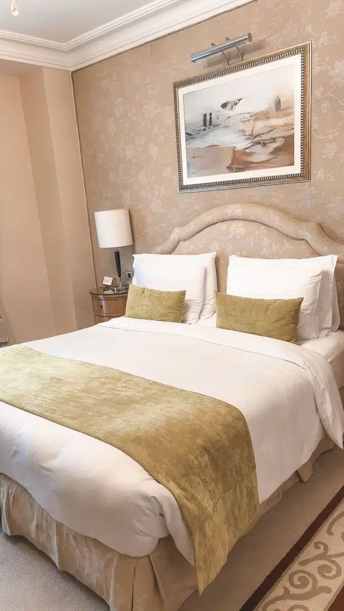 A king bed with cream and gold bedding and bedside lamps in a room at the Kempinski Nile Hotel, Cairo
