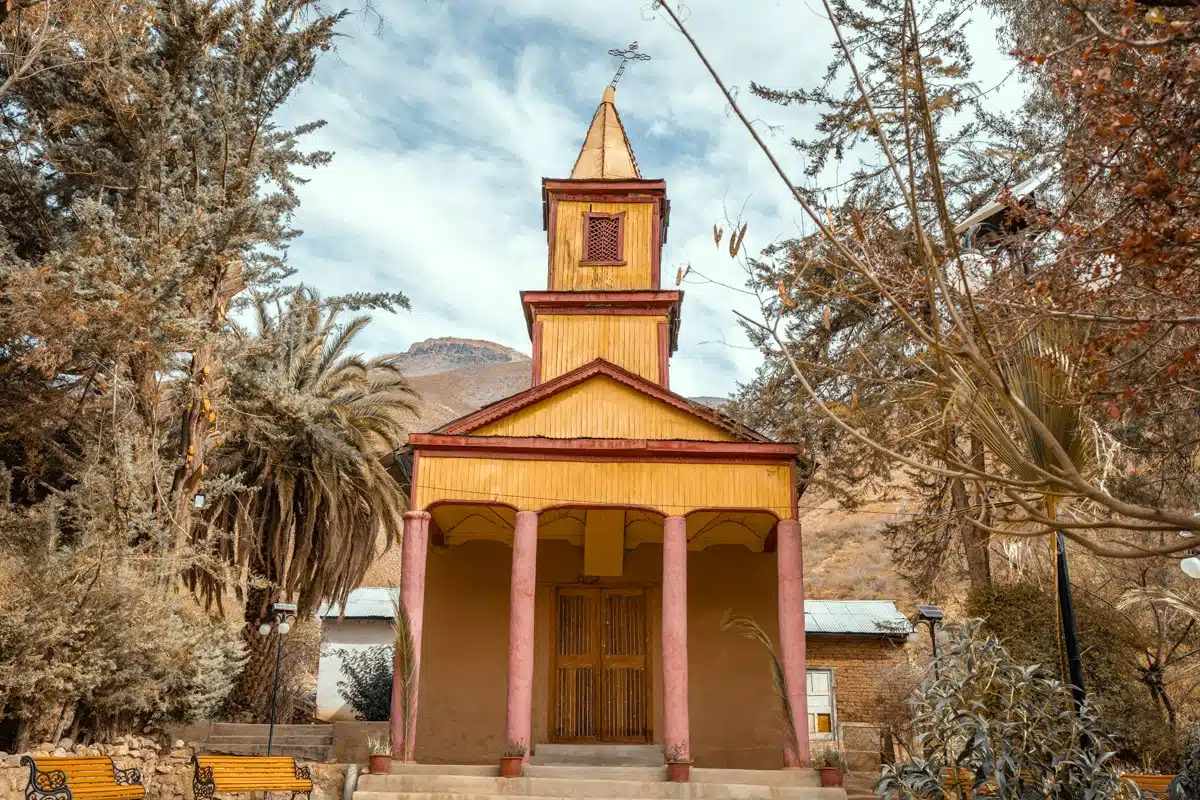 Small yellow wooden church with a bell tower among trees in the village of Alcohuaz, upper Elqui Valley