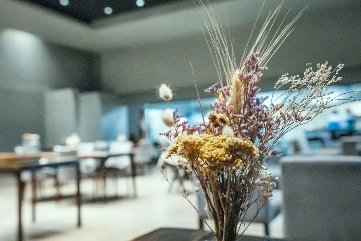 Dried flowers and wheat in a stone vase on a table, with Boragó's grey dining room behind