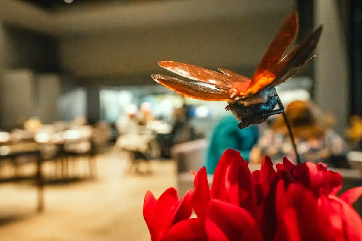 Copper winged insect sculpture on a stem above red cyclamen flowers in Boragó's dining room