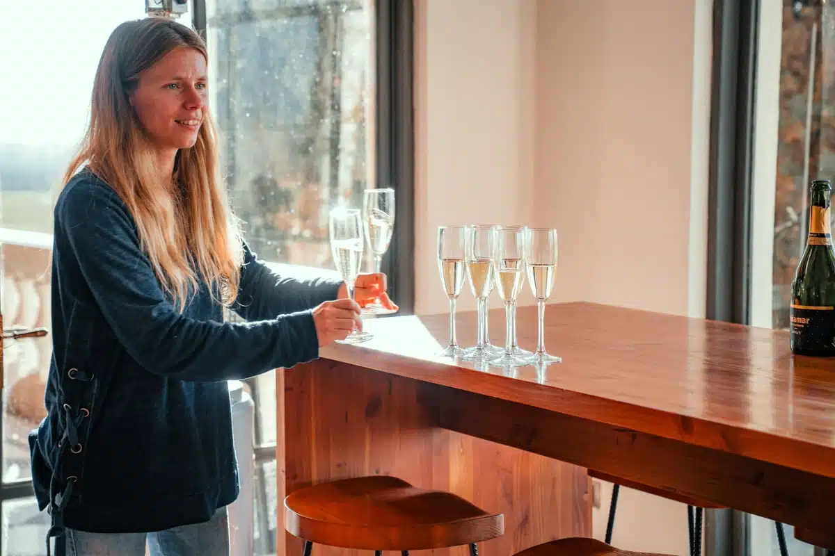Woman at a wooden tasting bar beside a row of sparkling wine flutes at Casa Viñamar, Casablanca