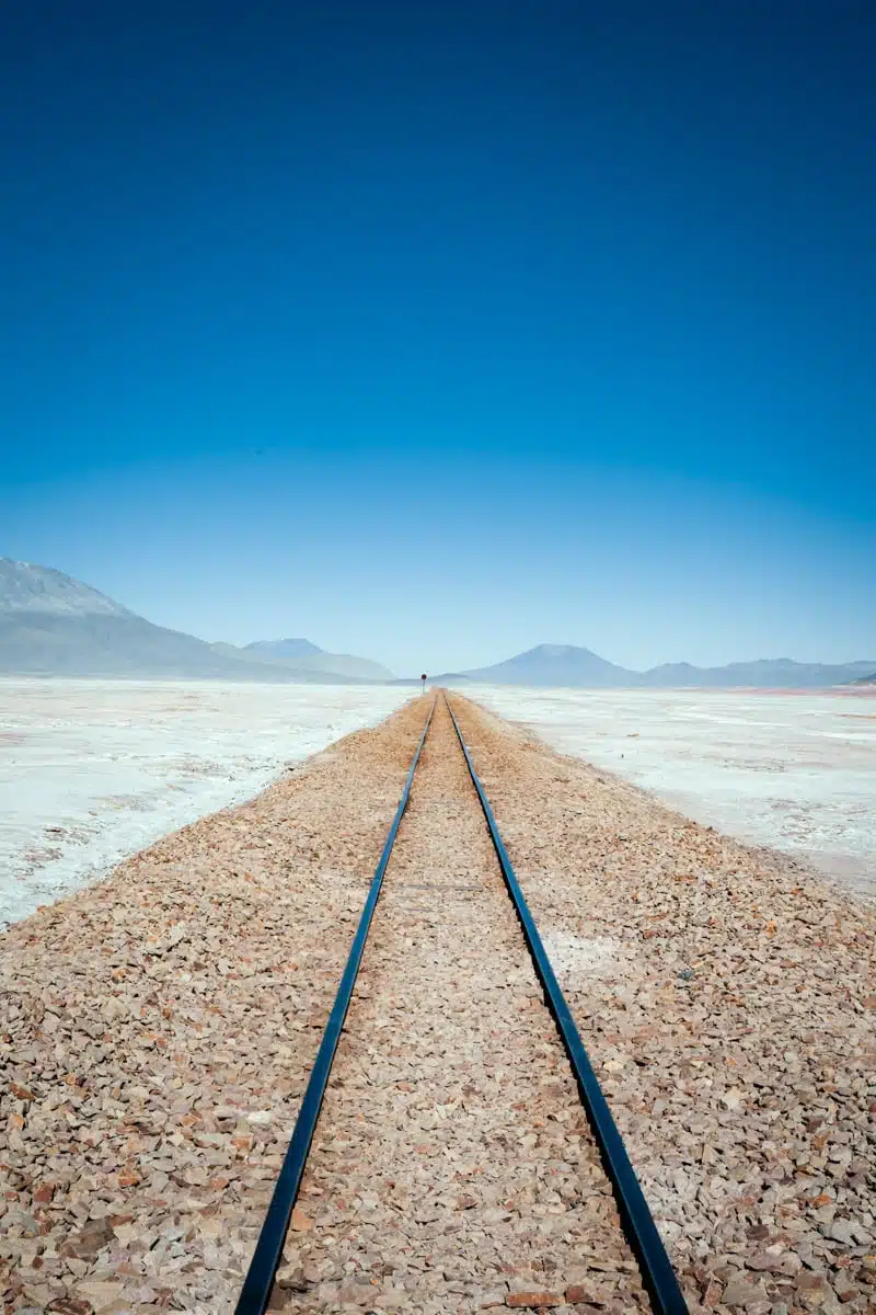 Straight railway track running across the white Chiguana salt flat in Bolivia towards distant hills