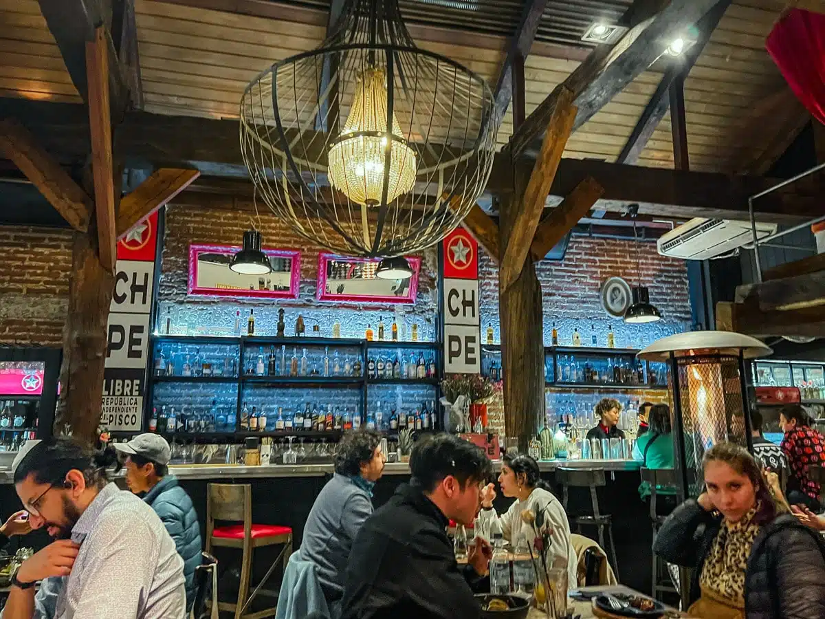 Diners at the bar of Chipe Libre in Lastarria beneath a large woven lantern and shelves of pisco