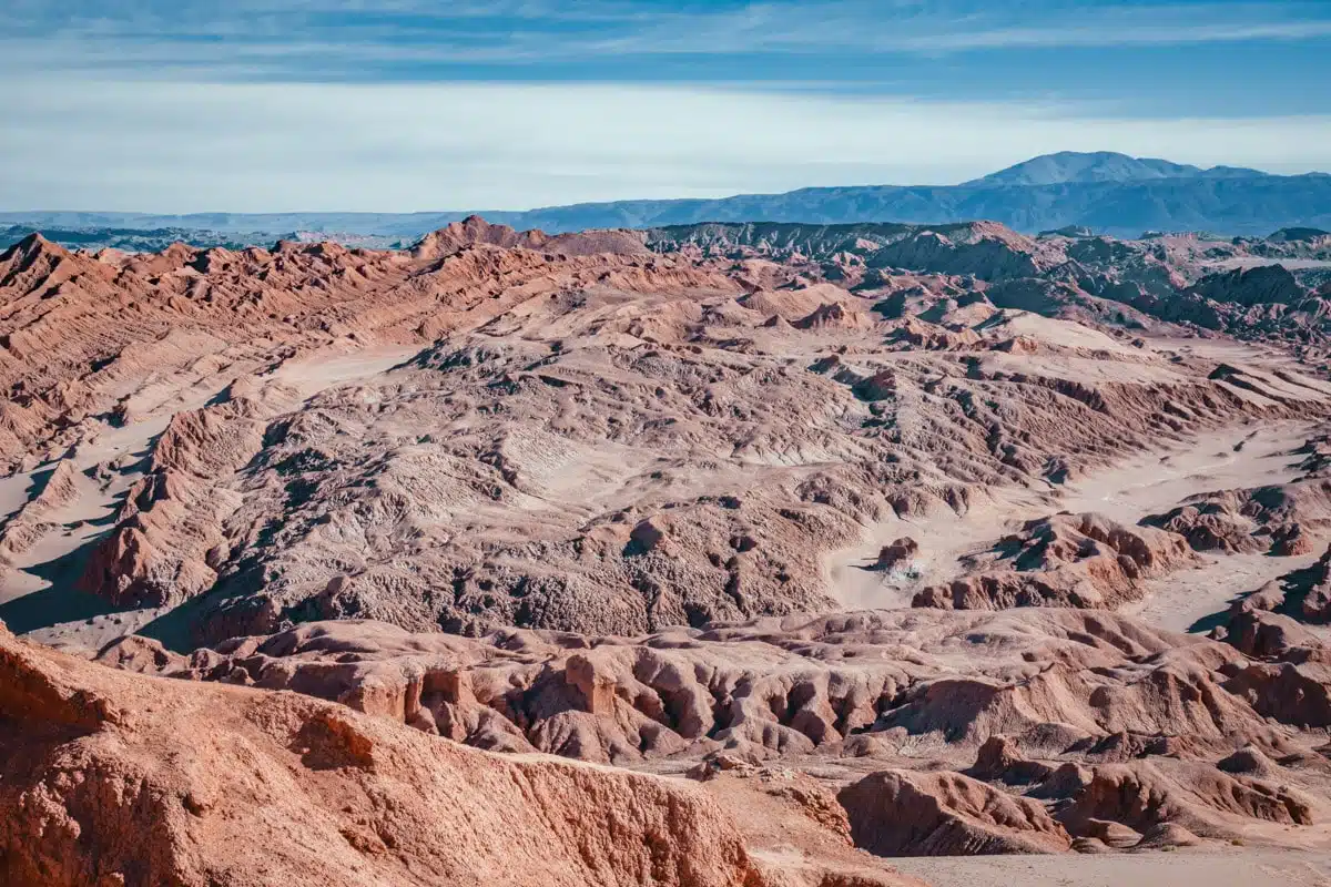 Red and cream eroded ridges of Ckamur rolling towards the salt flat and distant mountains in the Cordillera de la Sal