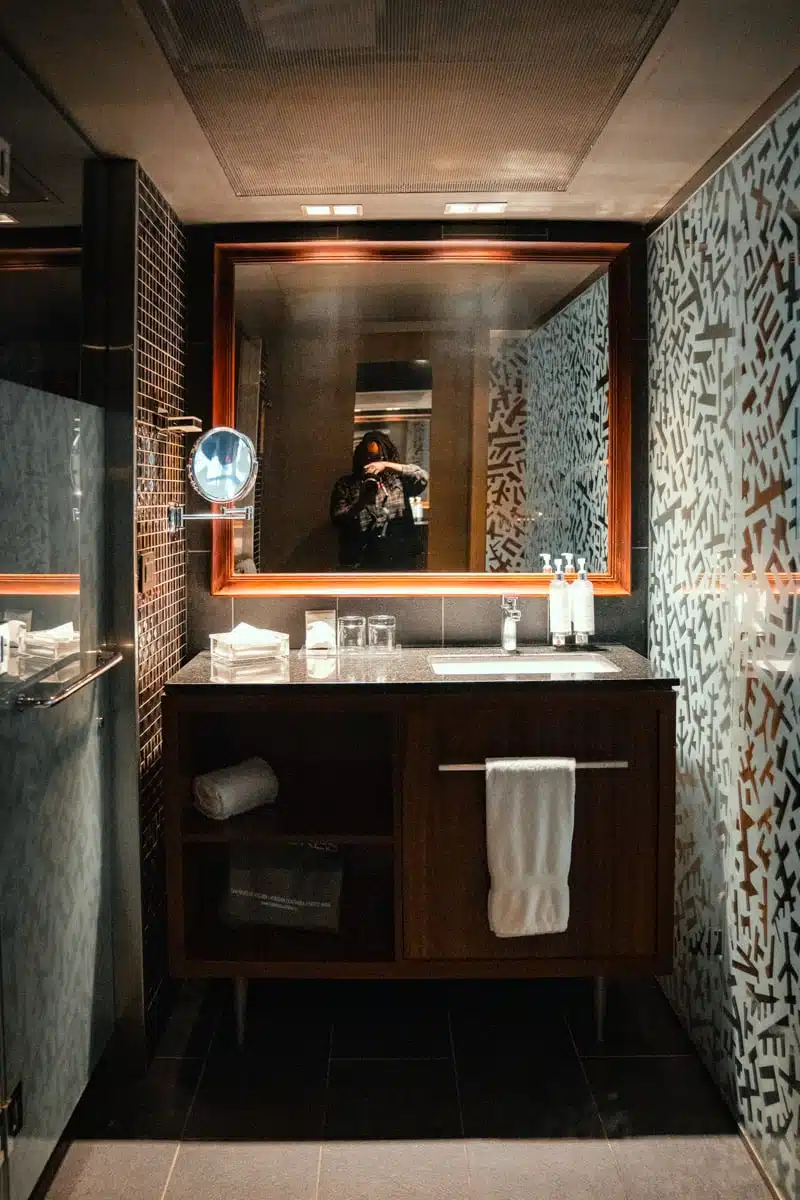 Mosaic-tiled bathroom with a dark wooden vanity, basin and lit mirror at Hotel Cumbres Lastarria