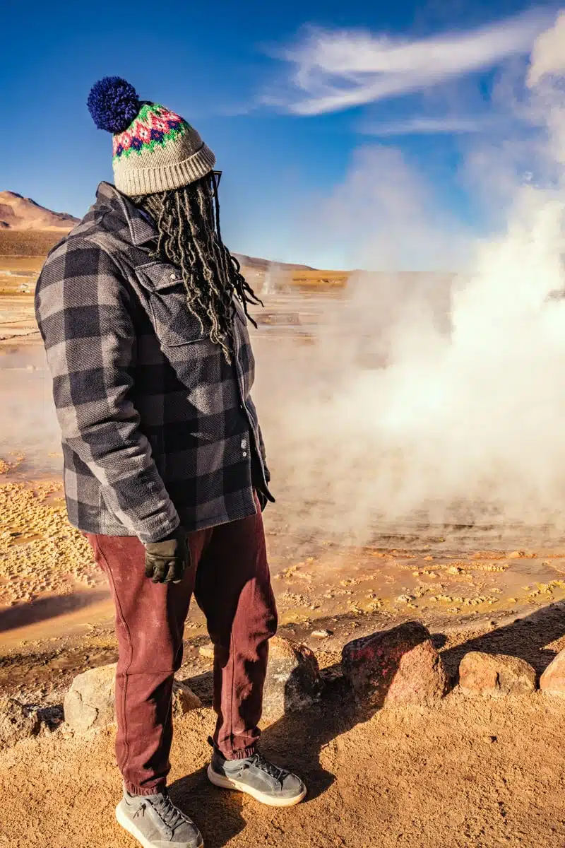 Julianna in a bobble hat and checked jacket watching steam rise at El Tatio geysers