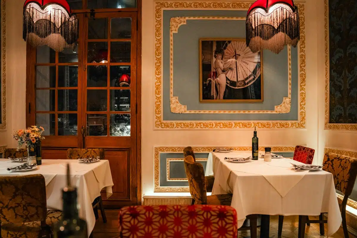 Liguria's dining room in Lastarria with fringed red lampshades, gilded mouldings, white tablecloths and a large framed photograph