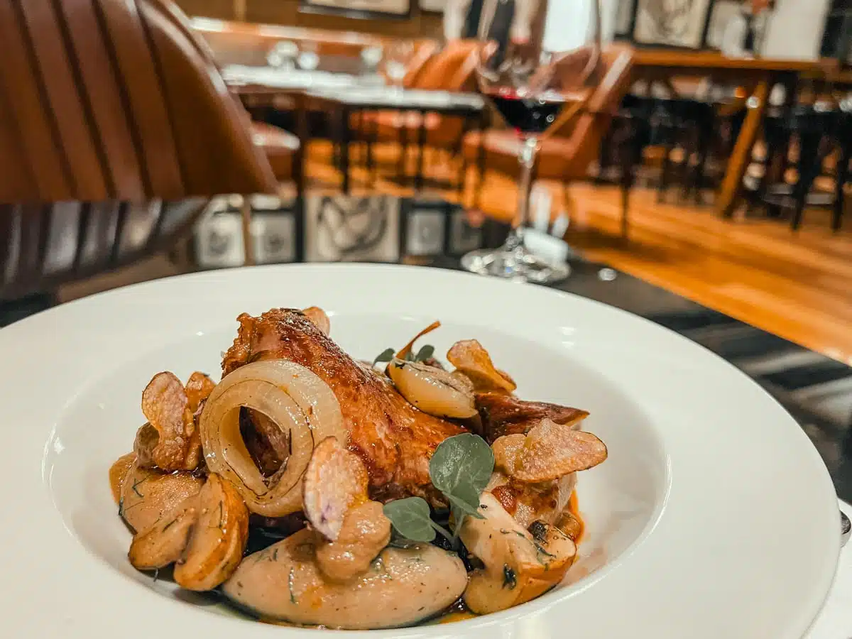 Plated main course with roasted onion and mushrooms beside a glass of red wine in The Singular restaurant
