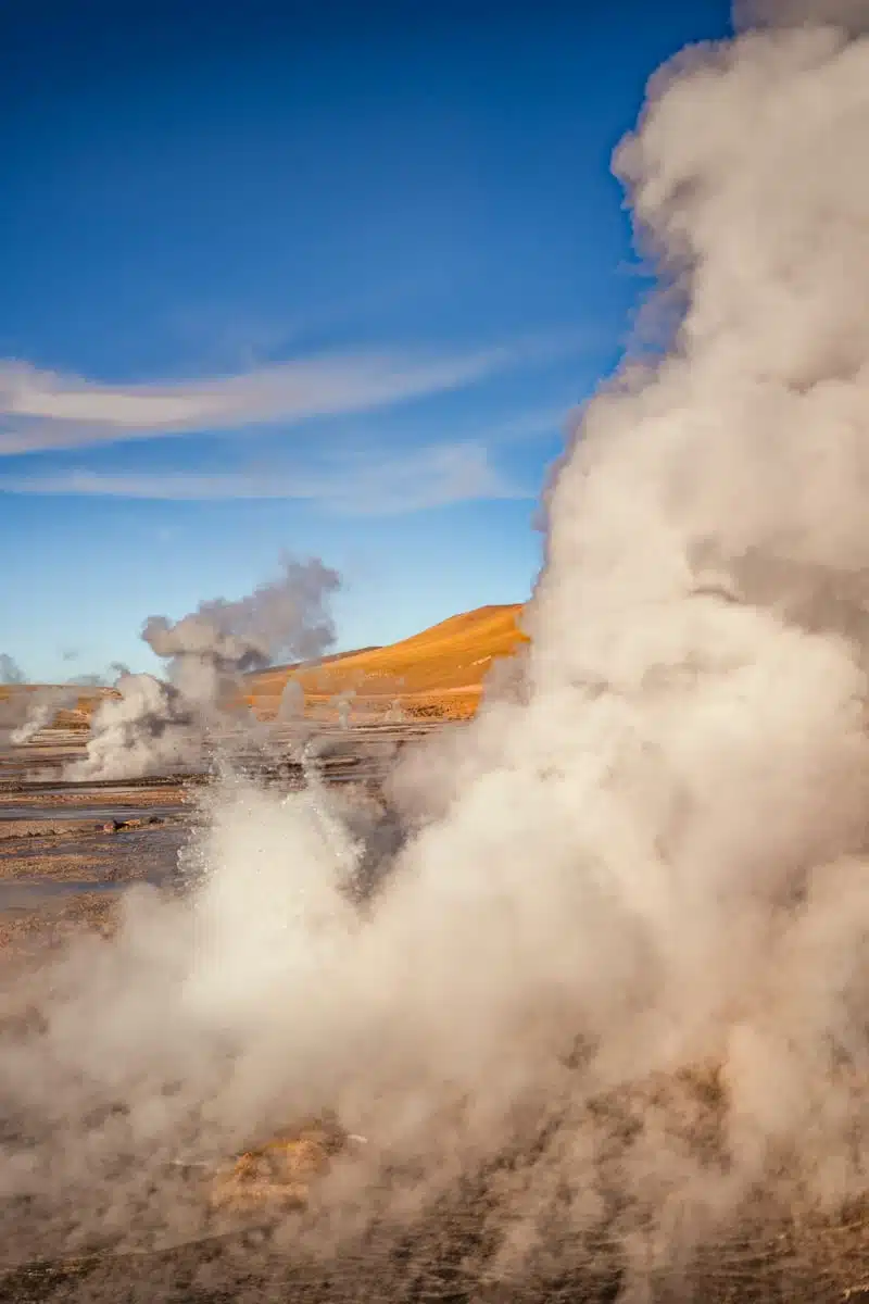 Thick white steam from fumaroles drifting across the El Tatio geyser field under blue sky