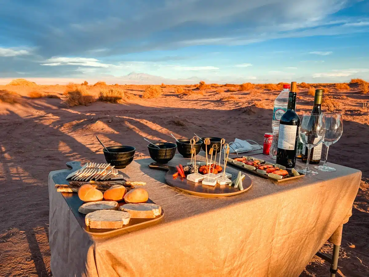 Table laid with wine, glasses, bread and canapés on red sand at sunset in the Atacama Desert
