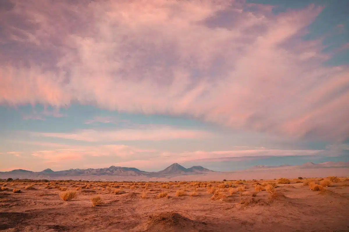 Low volcanoes on the horizon under a pink and blue evening sky over the red Atacama desert