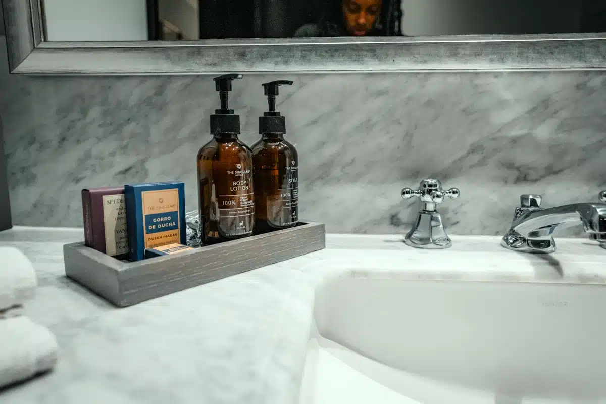 Marble bathroom basin with amber bottles of The Singular soap and body lotion on a wooden tray