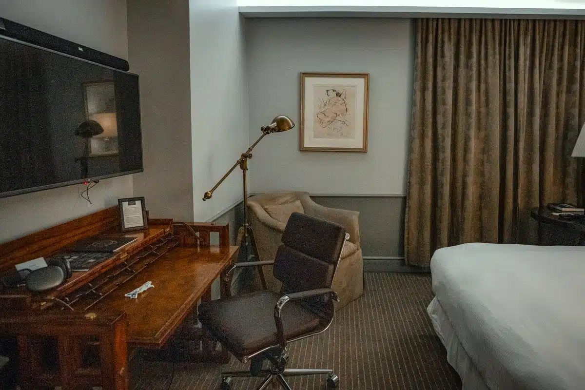 Guest room at The Singular Santiago with a wooden writing desk, brass lamp, armchair and bed