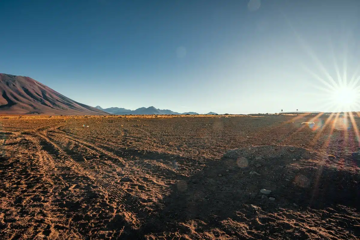 Early morning sun flaring over a mountain and the dusty altiplano at the Bolivia and Chile border