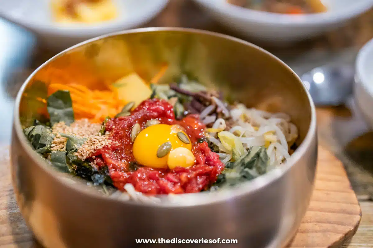 Jeonju-style bibimbap in a brass bowl topped with raw beef, an egg yolk, bean sprouts and vegetables