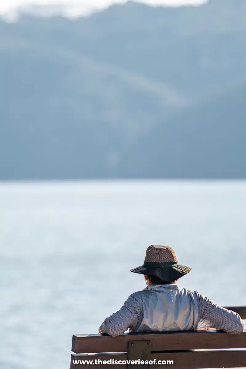 A visitor in a sun hat sitting on a bench looking out over the lake near Dosanseowon in Andong