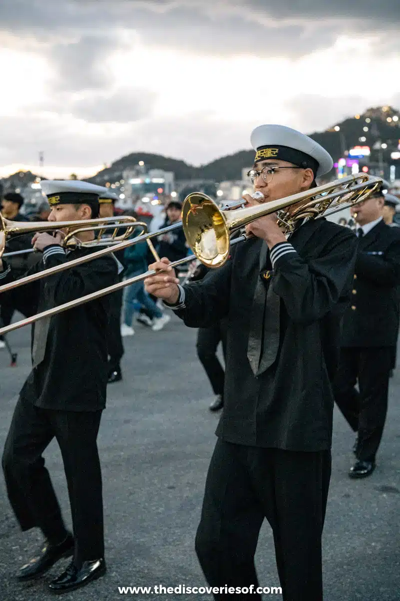 Naval bandsmen in white caps playing brass instruments as they march in the Mokpo Port Festival parade