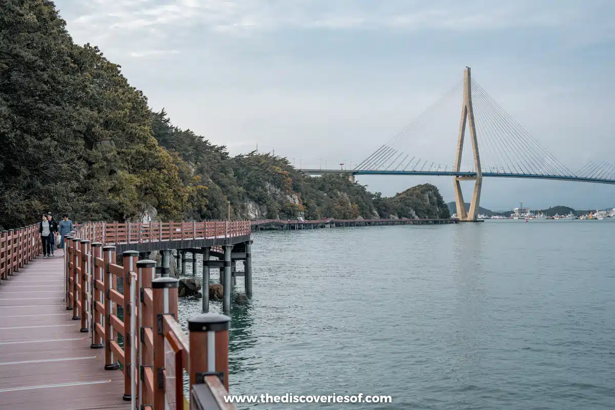 A wooden boardwalk with railings running along the cliffs of Gohado island towards Mokpo Bridge