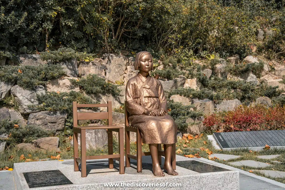 Bronze Statue of Peace of a girl in hanbok seated beside an empty chair in a garden in Mokpo