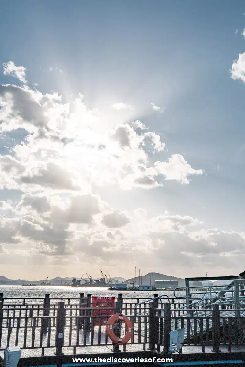 Sunbeams breaking through clouds above a railed pier and a red lifebuoy on the Mokpo waterfront
