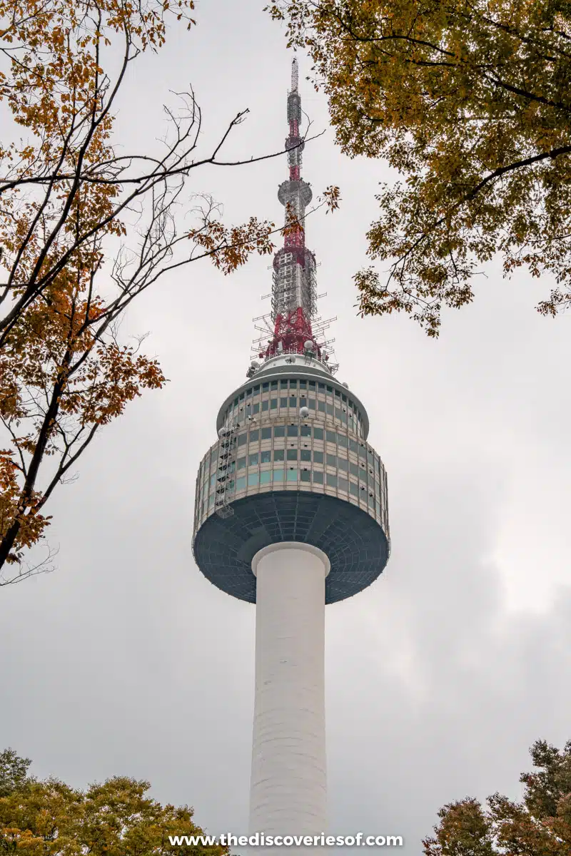 N Seoul Tower's white shaft and observation pod rising between autumn trees on the summit of Namsan in Seoul