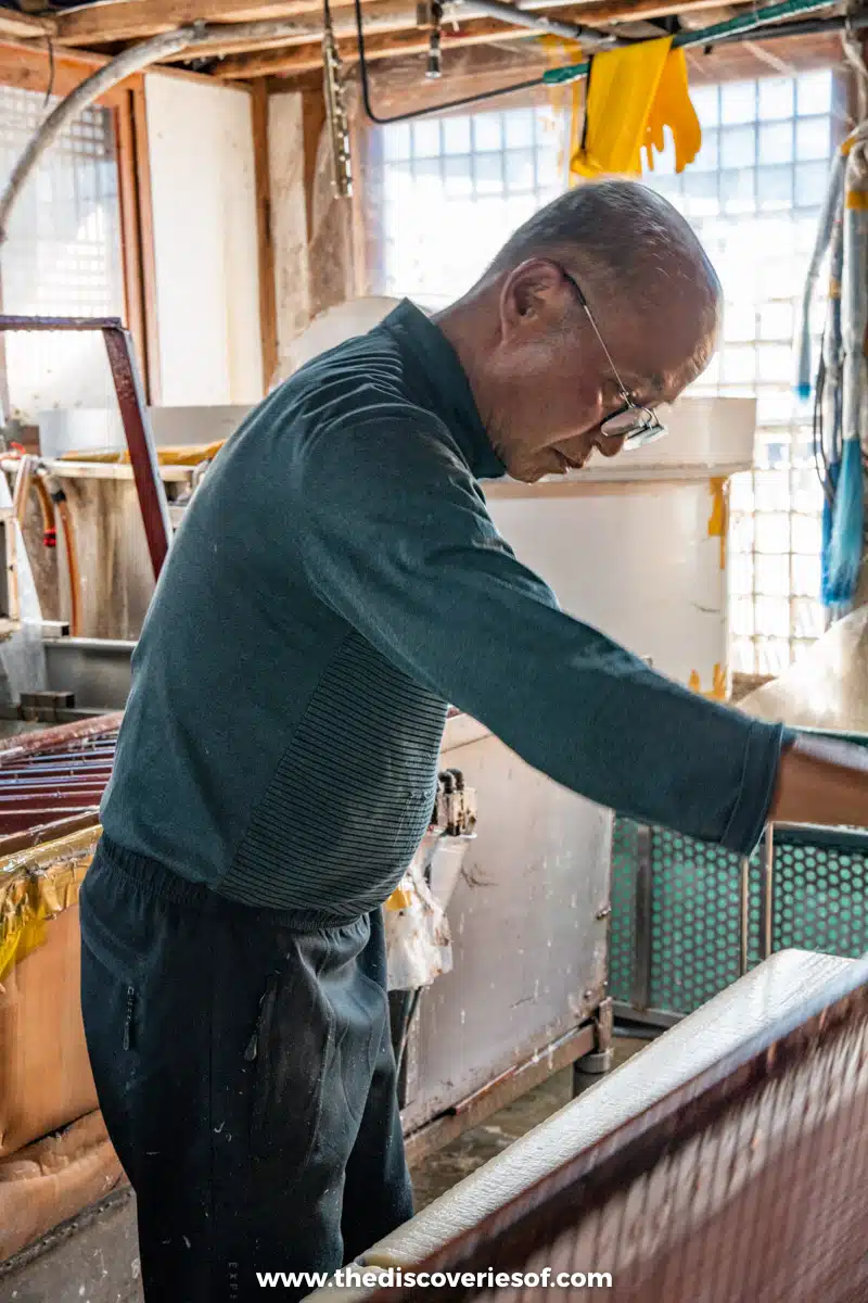 A papermaker leaning over a vat of pulp, forming sheets of traditional hanji paper in Jeonju