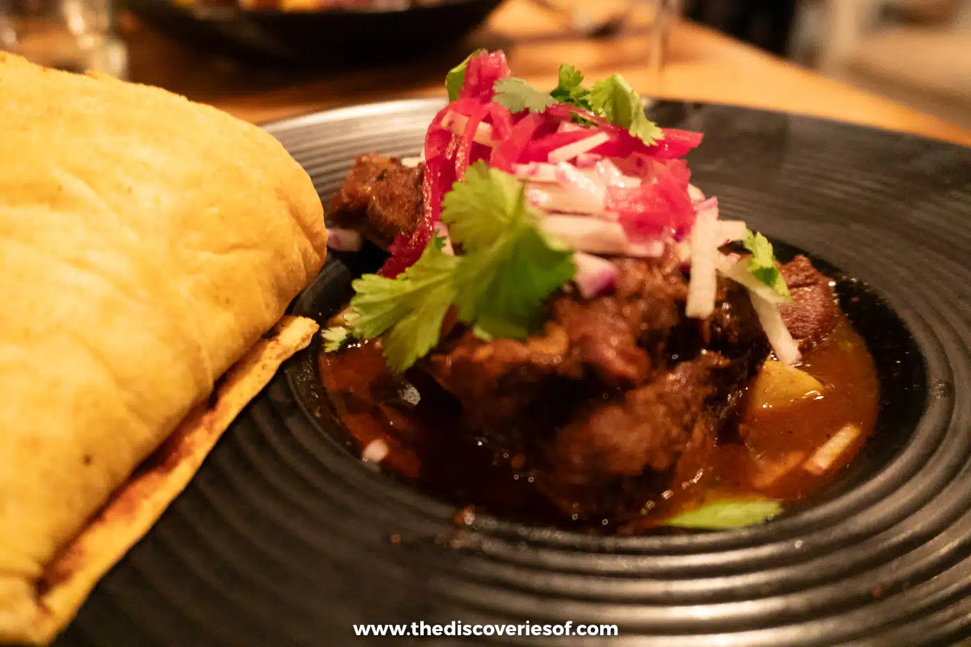 A plate of braised lamb birria topped with pickled onion and herbs with a tortilla at Campo at Los Poblanos