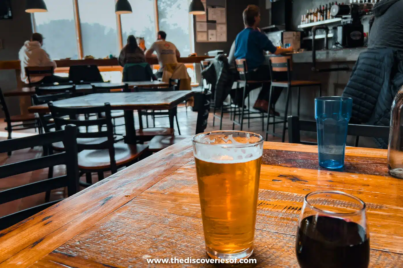 A pint of golden beer and a glass of red wine on a wooden table in an Albuquerque brewery taproom