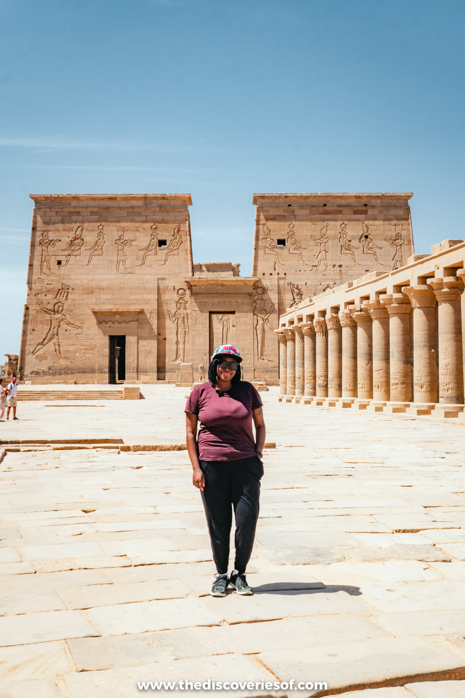 Julianna standing in the sunny forecourt of Philae Temple in Aswan in front of the first pylon and colonnade