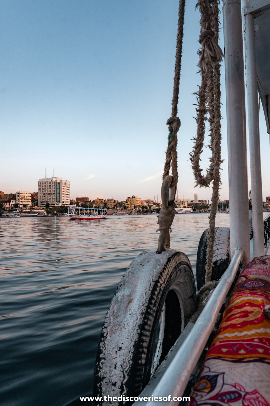 Ropes, a tyre fender and cushions on a motorboat on the Nile at dusk, with the Aswan skyline beyond