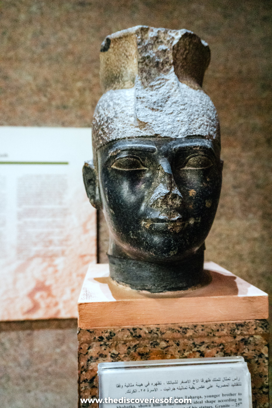 The dark granite head of a statue of the Kushite pharaoh Taharqa on a plinth in the Nubian Museum