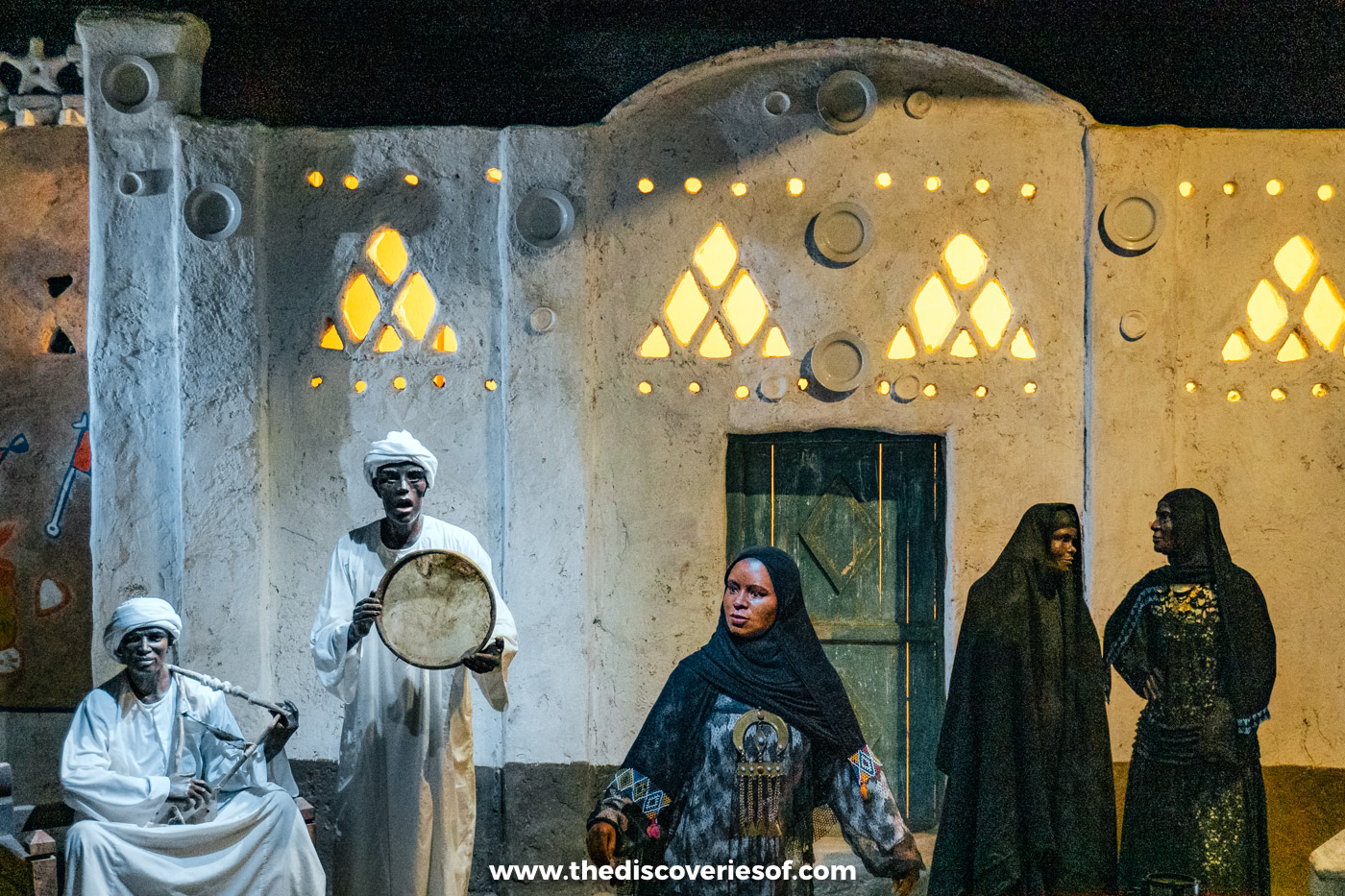 A life-size diorama of a Nubian village celebration with figures in white robes and black dresses, Aswan