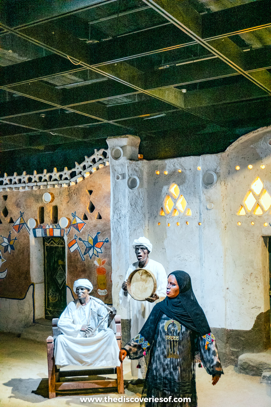 A diorama of Nubian villagers with a frame drum in front of a painted house in the Nubian Museum, Aswan