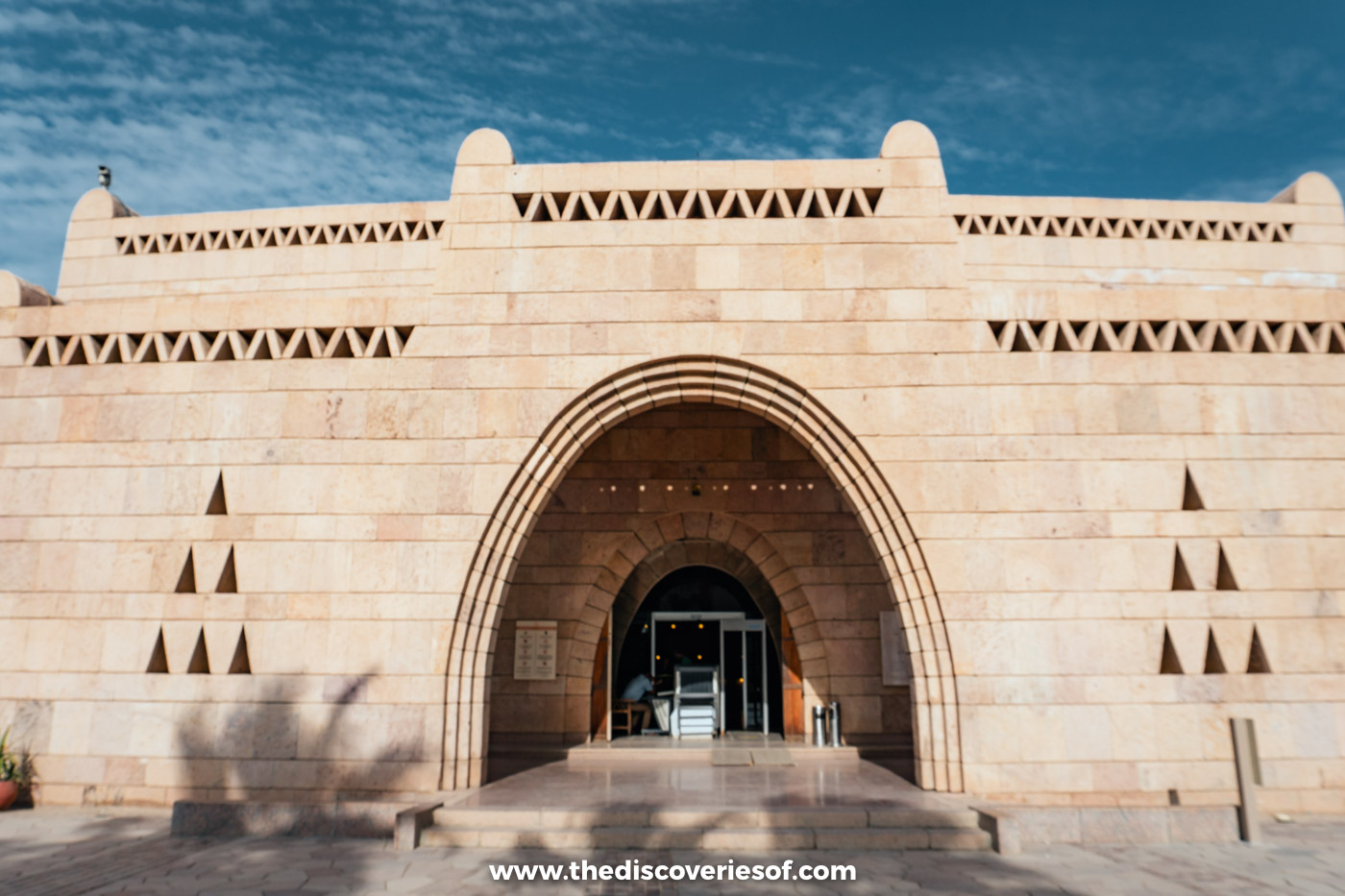 The arched sandstone entrance and decorated parapets of the Nubian Museum in Aswan under a blue sky