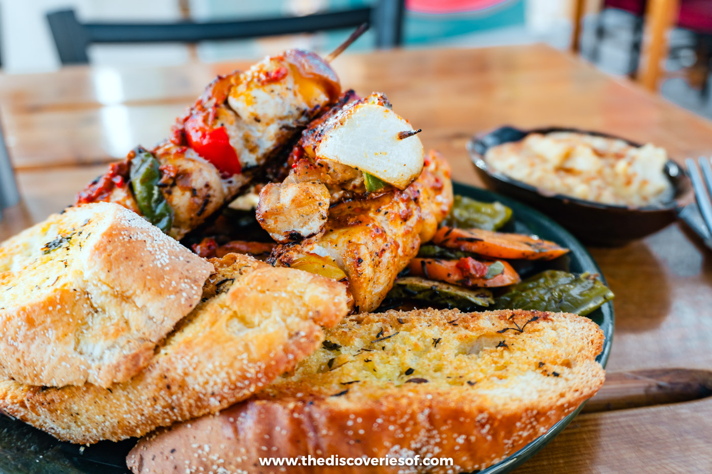 A plate of grilled meat and vegetable skewers with flatbread and dips on a table at Makani in Aswan
