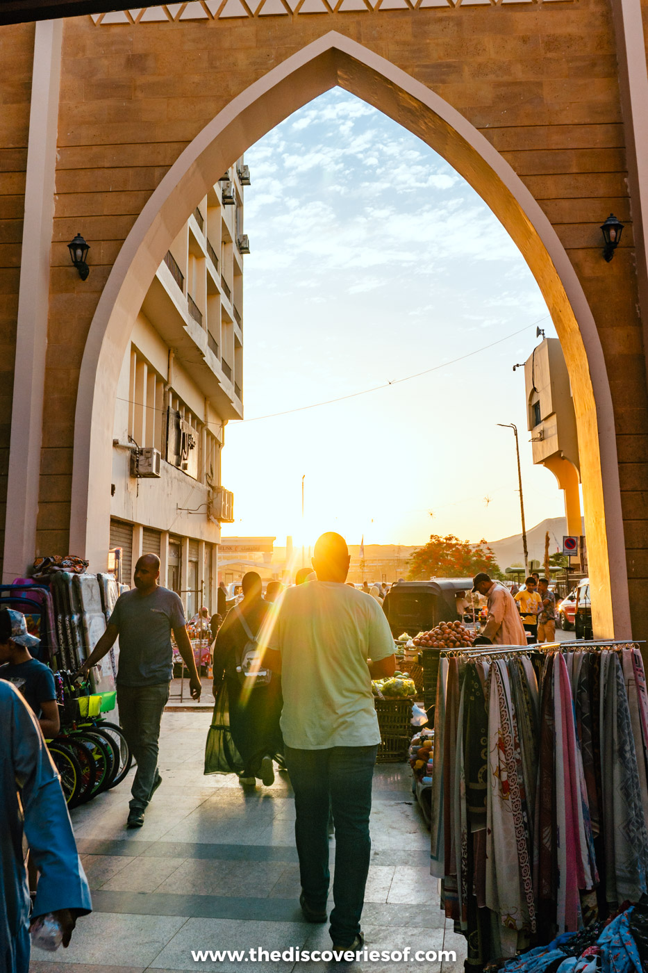 Shoppers walking through a tall pointed archway into the souq in Aswan as the sun sets behind it