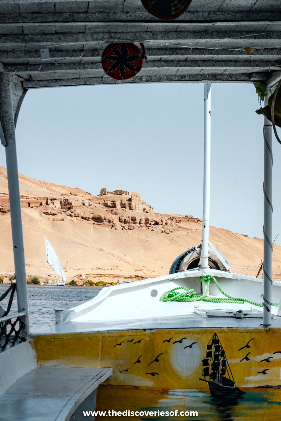The painted bow of a small motorboat heading across the Nile towards the desert cliffs of Aswan's West Bank
