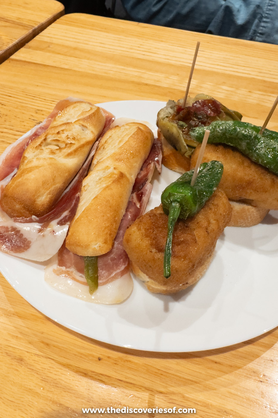 Two jamón bocadillos, a croquette pintxo and padrón peppers on a plate at the Mercado de la Ribera, Bilbao