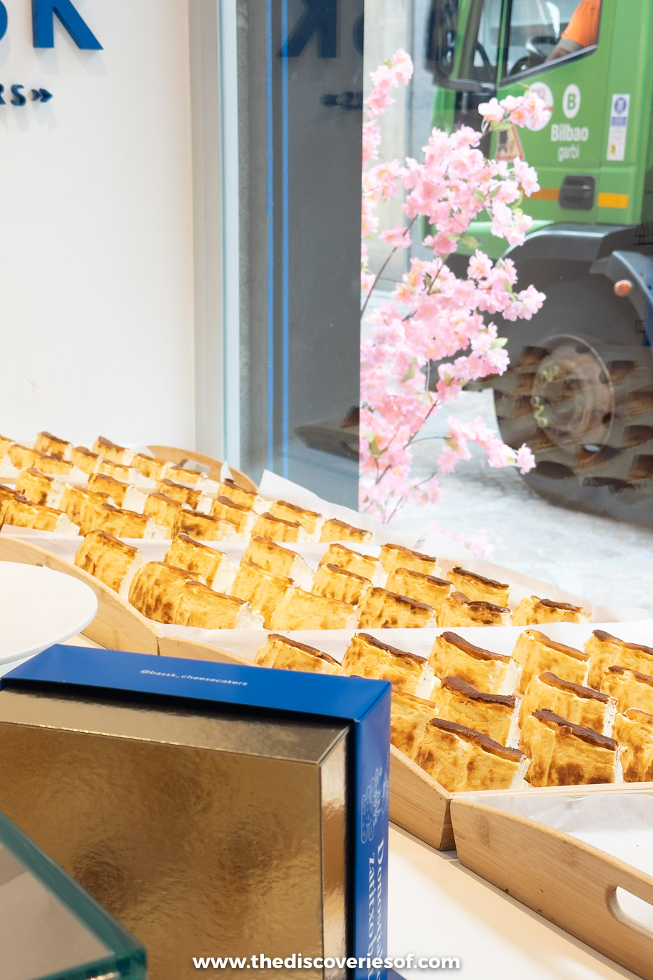 Rows of Basque cheesecake slices and a gold cake box in the window of Bassk Cheesecakers, Bilbao